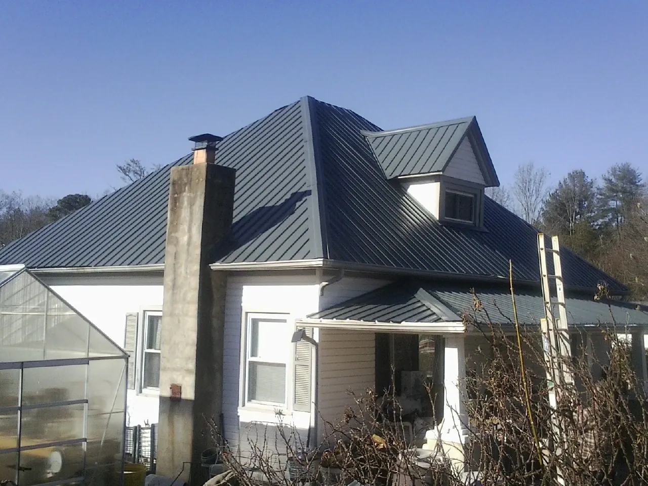 Dark blue standing seam metal roof on a white farmhouse with dormer — Slate & Tile Roof Repair by Roofing Brothers in Wakeman