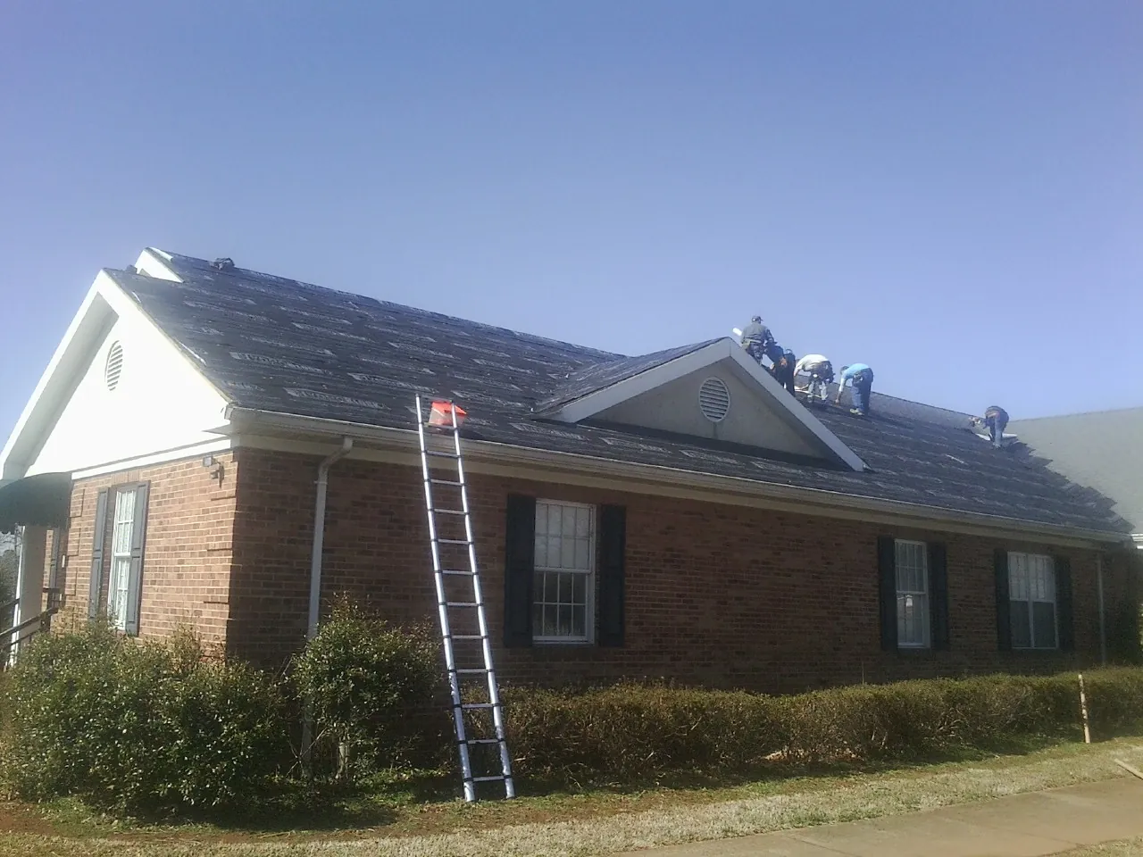 Crew tearing shingles off a brick ranch roof with a ladder set — Emergency Roof Repair work by our crew in Wakeman