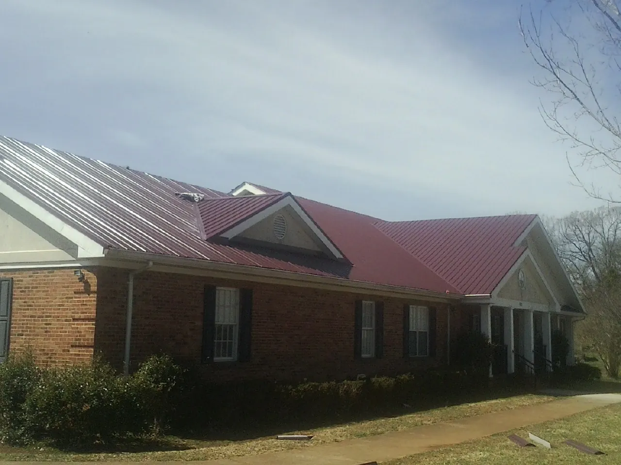 Red metal roof with gabled entries on a long brick building, from a Hail Damage Roof Repair job in Wakeman