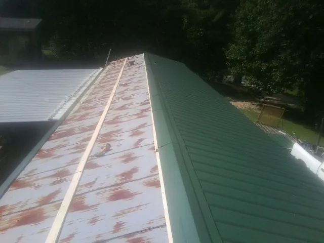 Old rusted panels beside newly installed green metal roofing — Wind Damage Roof Repair by Roofing Brothers in Wakeman