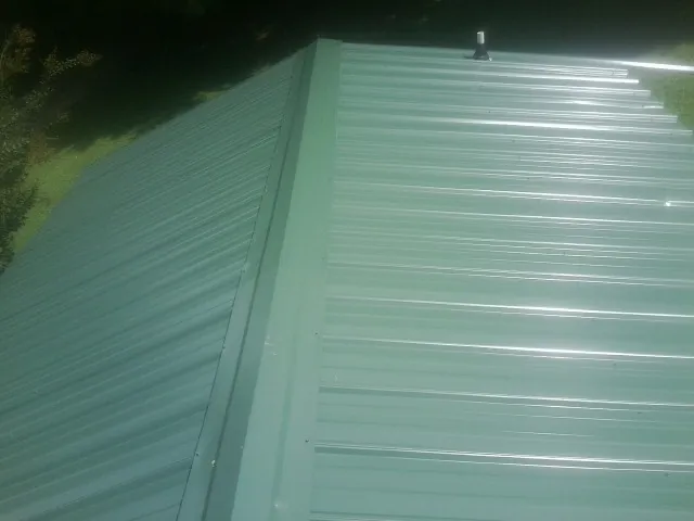 New green metal panels meeting at the ridge of a roof — Flat Roof Repair work by our crew in Wakeman