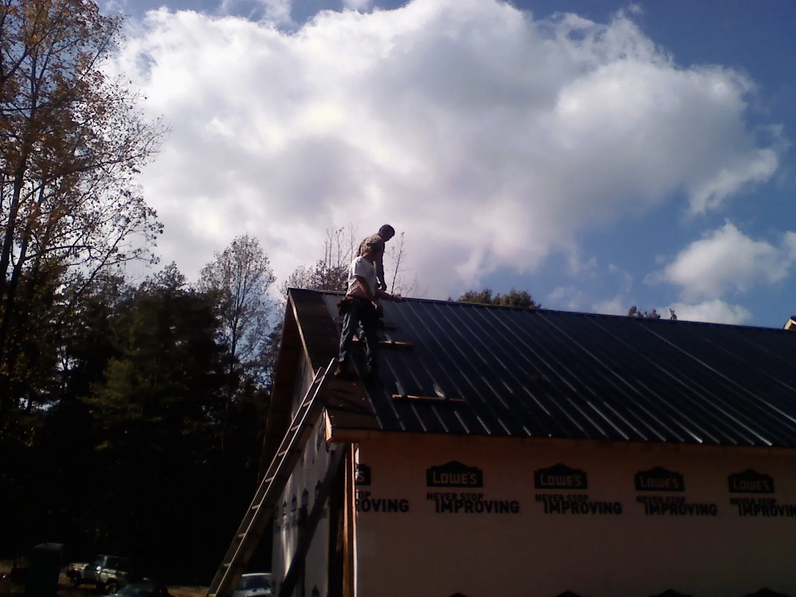 Roofer fastening dark metal panels high against a cloudy sky, from a Roof Inspection job in Wakeman