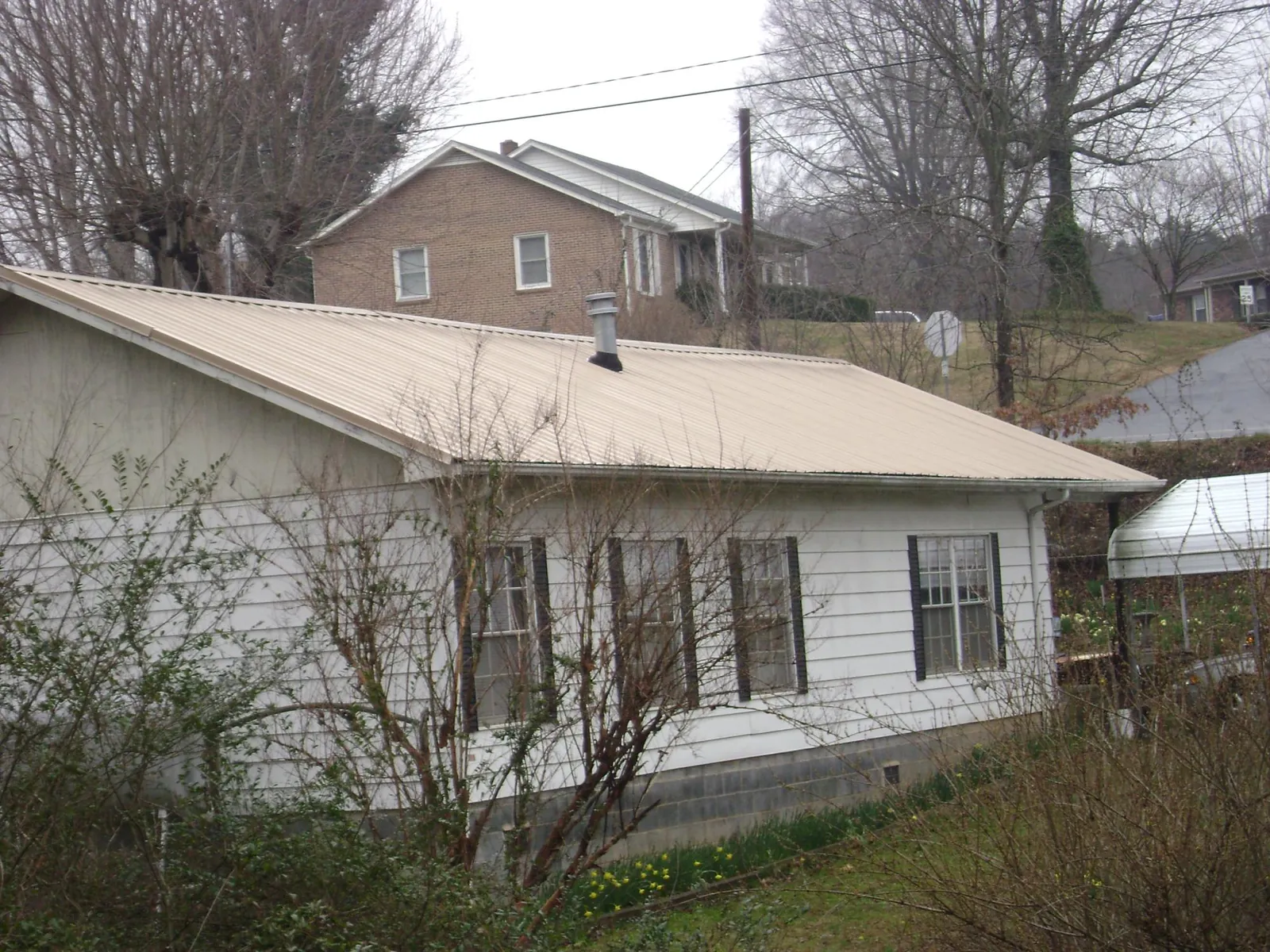 Tan metal roof on a white sided house set into a hillside — Commercial Roofing by Roofing Brothers in Wakeman