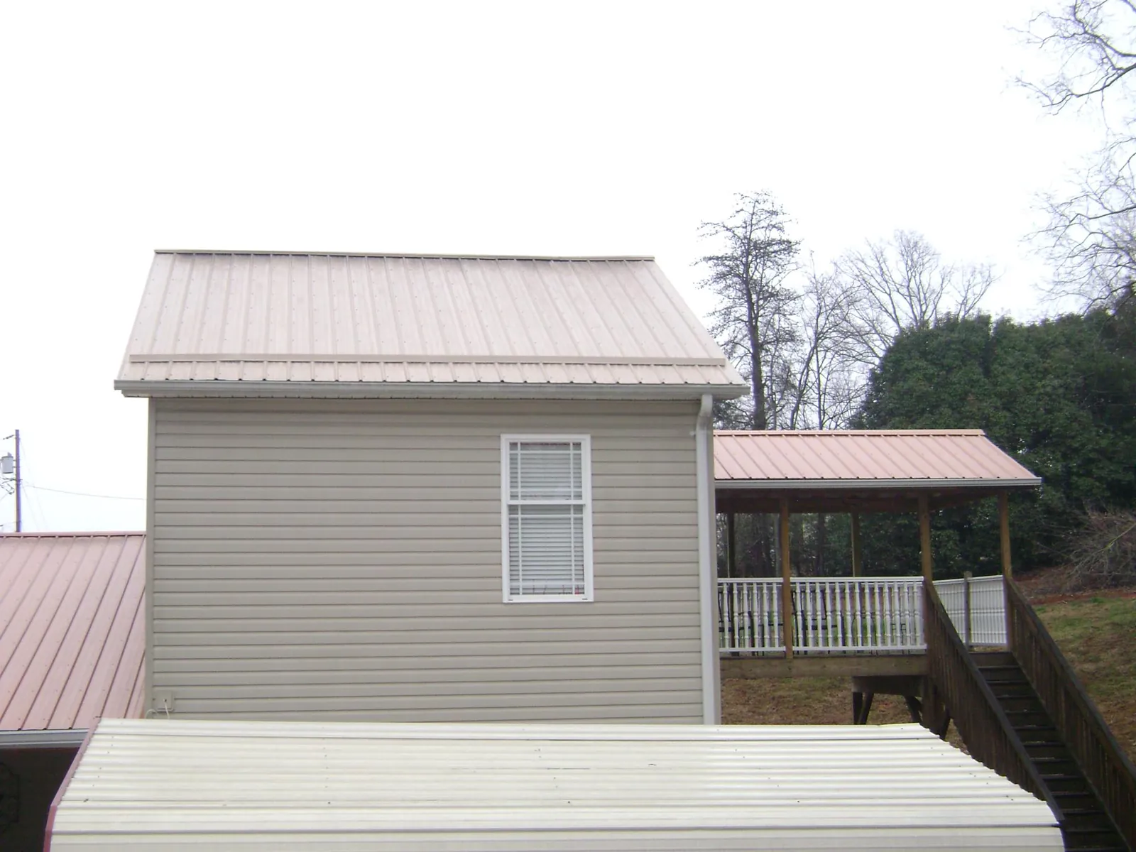 Tan metal roofs on a two story addition and attached porch, from a Roof Replacement job in Wakeman